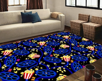 May include: A rectangular rug with a black background, patterned with blue film reels and red and white popcorn buckets. Yellow popcorn kernels are scattered across the design. The rug is in a living room setting.