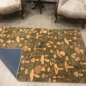May include: A green and brown area rug with a mushroom pattern. The rug has a brown border and a non-slip backing.