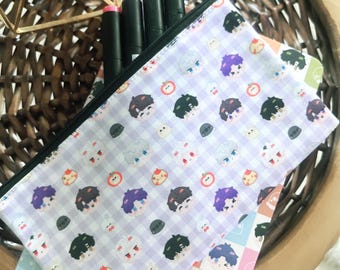 May include: A rectangular zippered pouch featuring a light purple and white gingham pattern decorated with small, colorful cartoon character faces and fruit icons. Several black markers with colored caps are tucked inside the pouch.
