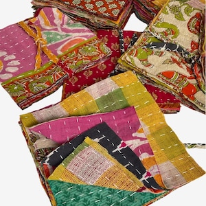 May include: A collection of folded fabric squares featuring various colorful patterns including floral, geometric, and animal motifs. Each piece is constructed from layered textiles held together by visible white running stitch embroidery.
