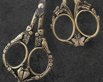 May include: Two pairs of ornate gold-toned scissors with floral and butterfly designs. The larger pair has the text "B.G.R." on the handle.