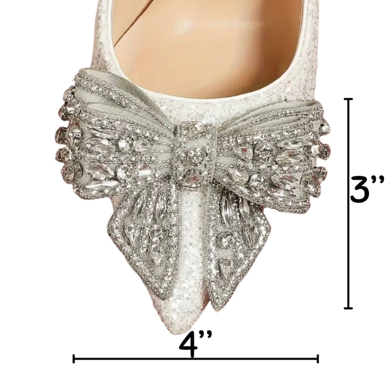 May include: White satin stiletto heels with a large silver bow embellished with rhinestones. The heels are 3 inches tall and the bow is 4 inches wide.