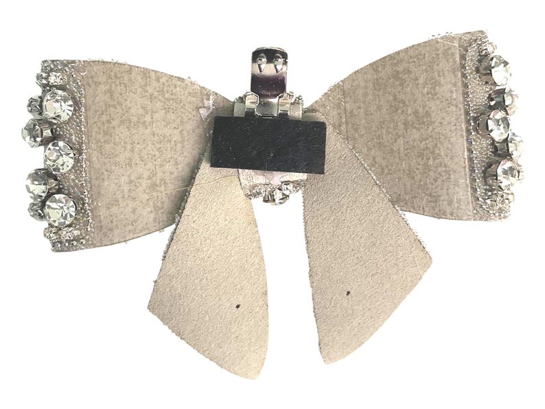 May include: A beige fabric bow with a silver metal clip and clear rhinestones. The bow is decorated with a silver glitter finish.