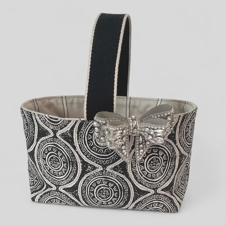 May include: A black and white patterned fabric tote bag with a black handle and a silver jeweled bow.