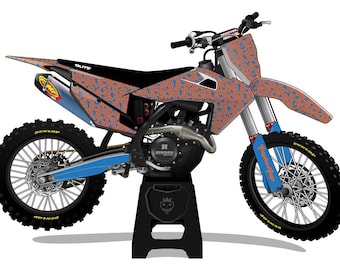 May include: A motocross bike with an orange and blue geometric pattern. The bike has black tires, a blue frame, and a black stand. The text "Dunlop" is visible on the tires.