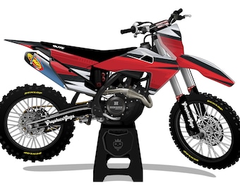 May include: A red, white, and black motocross motorcycle with black tires and gold rims. The motorcycle is on a black stand. The text "Graphics Guys" is visible on the frame. The tires have the text "Dunlop".