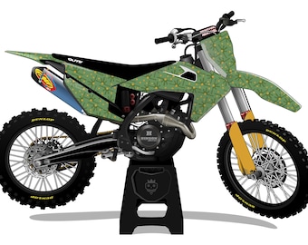 May include: A green and black dirt bike with a floral pattern on the body. The bike has black tires, a blue exhaust, and yellow accents. The bike is on a black stand.