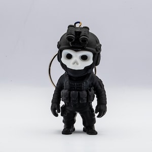 May include: A black figurine of a soldier wearing a helmet with night vision goggles and a skull-shaped mask. The soldier is dressed in tactical gear and has a keychain attachment. The figurine is set against a white background.
