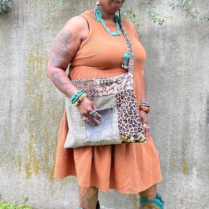 May include: A woman wearing a brown dress, a brown hat, and brown cowboy boots. She is carrying a patchwork bag with a denim pocket and animal print fabric. She is wearing turquoise jewelry.