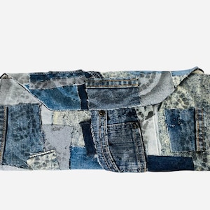May include: A patchwork denim clutch in various shades of blue. The rectangular bag features a flap closure and is constructed from repurposed denim pieces, including a small pocket. The design showcases a mix of textures and washes.