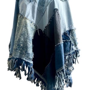 May include: A patchwork poncho constructed from various shades of blue denim fabric. The garment features a mix of light, medium, and dark wash denim panels with visible frayed seams and edges, finished with a long, uneven fringe along the hemline.