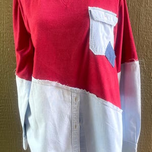 May include: A red and light blue long-sleeve shirt. The top half is red, and the bottom half is light blue, with a denim pocket and a blue diamond-shaped patch. The shirt has a raw, unfinished hemline.