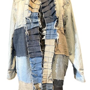 May include: A patchwork denim jacket with a light blue wash. The jacket features a variety of denim patches in shades of blue, gray, and tan. The front has a layered, ruffled design. The jacket has a button-down closure and long sleeves.
