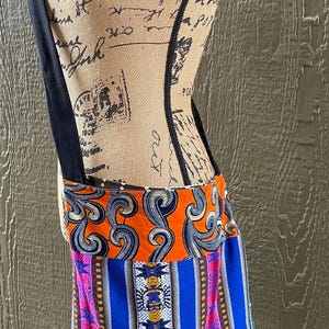 May include: A colorful fabric tote bag with a black strap. The bag has a blue, orange, and white patterned design.