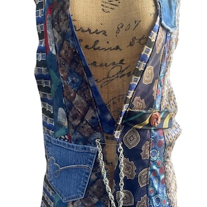 May include: A patchwork vest constructed from various patterned neckties, featuring denim pocket details and a silver chain closure. The vest showcases a mix of blue, red, and brown tie designs, creating a unique and eclectic style.