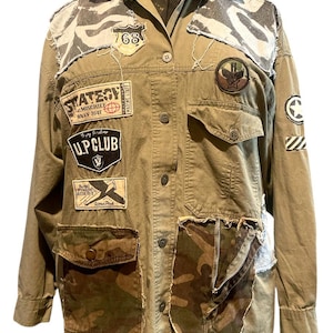 May include: Olive green jacket with multiple patches and camouflage accents. Features a button-up front, two chest pockets, and two lower pockets. Patches include text and military-style emblems. Distressed fabric details add a vintage aesthetic.