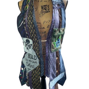 May include: A patchwork vest made from various patterned neckties in shades of blue, brown, and green. The vest features a small pocket with a floral design and patches with text that reads "BOLD IN MY OWN SKIN".