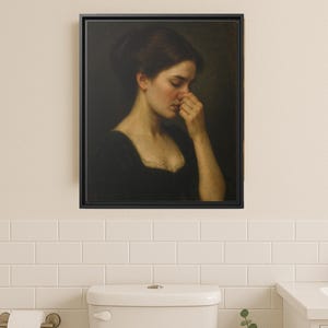 May include: A framed painting of a woman in a black dress, with her hand on her face. The artwork is set against a dark backdrop. The painting is displayed in a bathroom with a white toilet, sink, and a small potted plant.