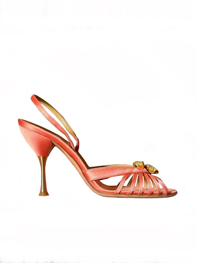 Puede incluir: Sandalia de sat&eacute;n color coral con tac&oacute;n fino y tiras delicadas. El zapato de punta abierta presenta un tac&oacute;n dorado y un adorno decorativo en la pala. La altura del tac&oacute;n es de aproximadamente 9 cm.