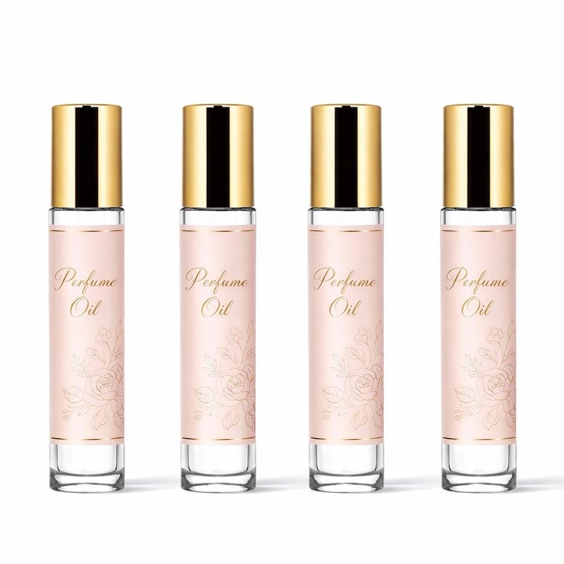 Op de afbeelding: Vier parfumolieflessen met gouden doppen en heldere glazen lichamen. Elke fles heeft een roze etiket met gouden tekst "Perfume Oil" en een bloemenontwerp. De flessen zijn in een rij gerangschikt.