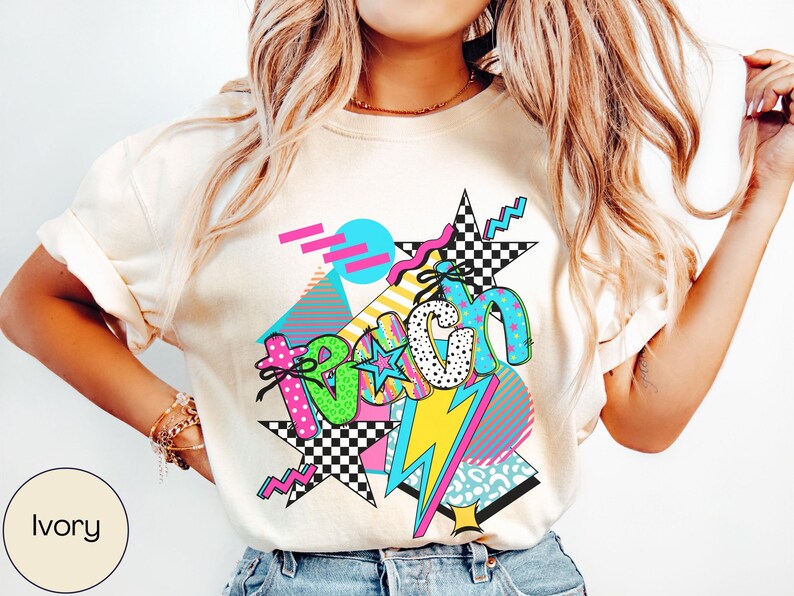 Puede incluir: Camiseta de color marfil con un dise&ntilde;o gr&aacute;fico colorido. El dise&ntilde;o presenta la palabra "Beach" en una fuente retro, con estrellas, rayos y formas geom&eacute;tricas en rosa, verde, azul y amarillo. La camiseta es de estilo casual.