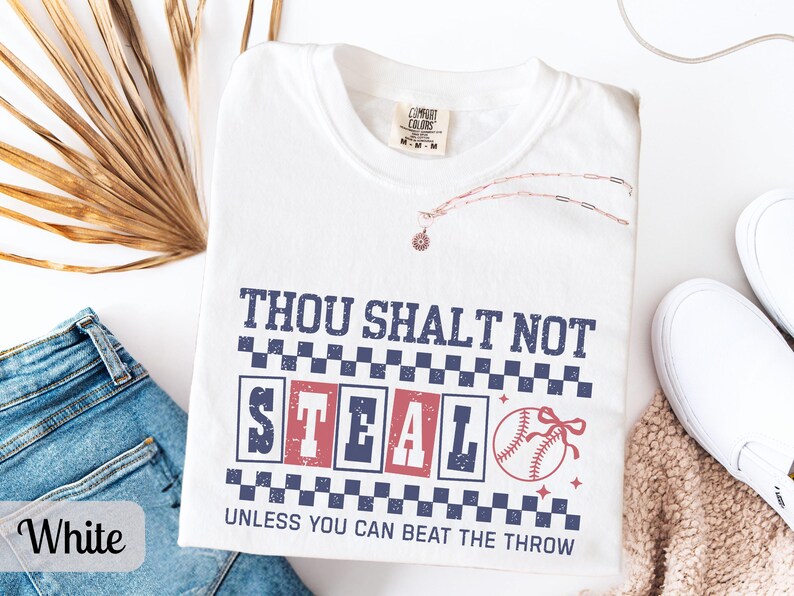 May include: White t-shirt with the text "THOU SHALT NOT STEAL UNLESS YOU CAN BEAT THE THROW" in navy blue and red. A baseball graphic is on the right. The shirt is surrounded by blue jeans, white shoes, and a necklace.