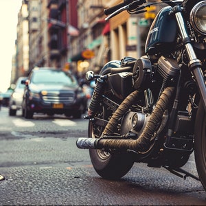 May include: A black motorcycle parked on a city street. The motorcycle has a chrome headlight and a black leather seat. The motorcycle is in focus, while the background is blurred.