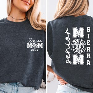May include: Dark gray sweatshirt with white text. The front features "Senior Mom 2027" with a pom-pom graphic. The back displays "Mom Sierra 2027" in a vertical and stacked design, also with a pom-pom graphic.