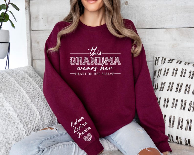 May include: Burgundy sweatshirt with the text "This Grandma wears her heart on her sleeve" and the names "Calvin, Karissa, Jessica" on the sleeve.