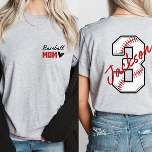May include: Two gray t-shirts. One shirt has the text "Baseball Mom" with a black heart. The other shirt has a white baseball with red stitching and the number "3" with the text "Jackson" in red.