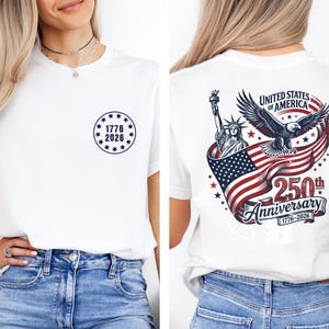 Pode incluir: Camiseta branca com um design circular azul marinho na frente, com o texto "1776 2026". A parte de tr&aacute;s da camisa exibe um gr&aacute;fico patri&oacute;tico com o texto "United States of America 250th Anniversary 1776-2026", com uma &aacute;guia e a Est&aacute;tua da Liberdade.