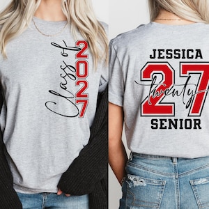 May include: A light gray t-shirt with the text "Class of 2027" in black script and red block letters. The back of the shirt features the name "Jessica", the number "27", and the word "Senior".