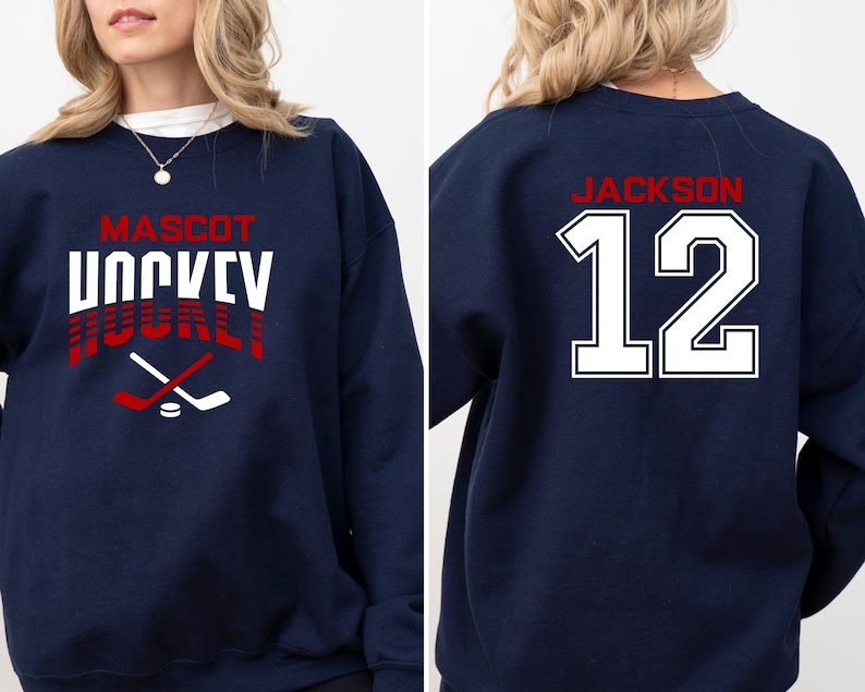 K&ouml;nnte beinhalten: Ein marineblauer Sweatshirt mit dem Text "MASCOT HOCKEY" in Rot und Wei&szlig; auf der Vorderseite und dem Text "JACKSON 12" in Wei&szlig; auf der R&uuml;ckseite.