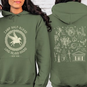 May include: A green hooded sweatshirt with a white graphic on the front that says "Camp Half-Blood Long Island Sound -New York-." The back of the sweatshirt has a white graphic of various symbols, including a pegasus, a lyre, a sword, a tree, and a building.