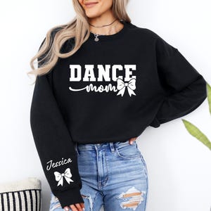 Pu&ograve; includere: Felpa nera con la scritta "Dance Mom" e un fiocco bianco. La felpa ha un fiocco bianco e il nome "Jessica" sulla manica.