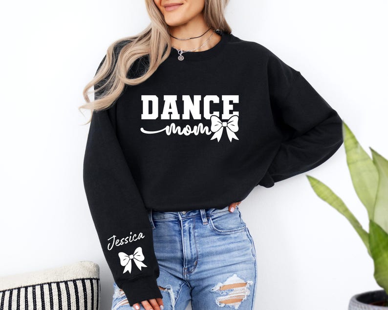Pu&ograve; includere: Felpa nera con la scritta "Dance Mom" e un fiocco bianco. La felpa ha un fiocco bianco e il nome "Jessica" sulla manica.