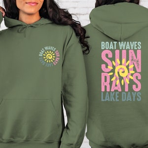 May include: A green hooded sweatshirt with a graphic design on the front and back. The design features a yellow sun with the words "Boat Waves Sun Rays Lake Days" in a circle around it. The back of the sweatshirt has the same design but with the words "Boat Waves" at the top and "Lake Days" at the bottom.