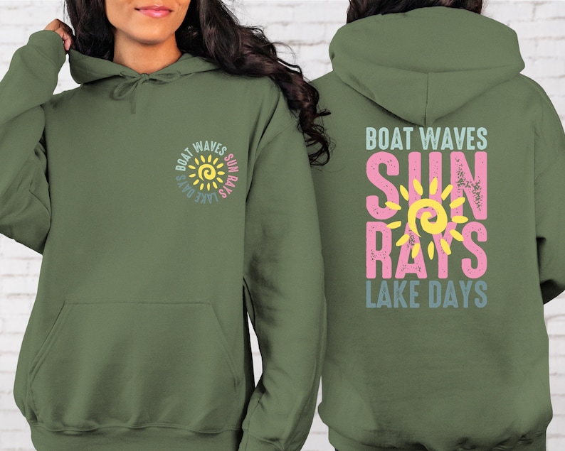 May include: A green hooded sweatshirt with a graphic design on the front and back. The design features a yellow sun with the words "Boat Waves Sun Rays Lake Days" in a circle around it. The back of the sweatshirt has the same design but with the words "Boat Waves" at the top and "Lake Days" at the bottom.
