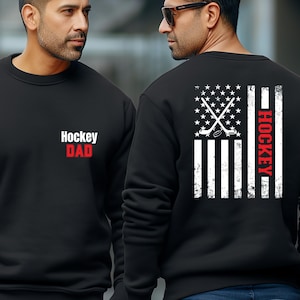May include: Two black sweatshirts with a white American flag design. One sweatshirt has the text "Hockey Dad" on the front. The other sweatshirt has the text "Hockey" on the side of the flag.