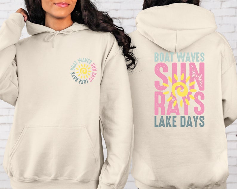 May include: A cream-colored hoodie with a sun graphic and the text "Boat Waves Sun Rays Lake Days" on the front and back. The sun graphic is yellow with orange rays and a blue outline. The text is in a blue, pink, and yellow color scheme.