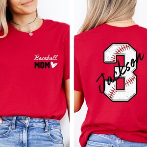 May include: Two red t-shirts. One says "Baseball Mom" with a heart. The other has a white baseball with the number 3 and the name "Jackson" written on it.