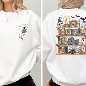 May include: White sweatshirt with a ghost reading a book on the front and a bookshelf with Halloween decorations on the back.