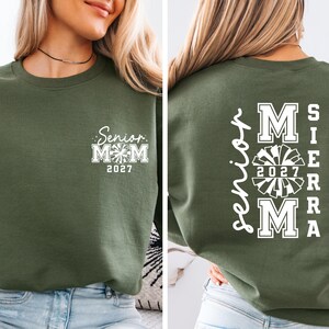 May include: Olive green sweatshirt with white text. The front features "Senior Mom 2027" with a cheerleader graphic. The back displays "Sierra Mom 2027" in a vertical and stacked layout, also with a cheerleader graphic.