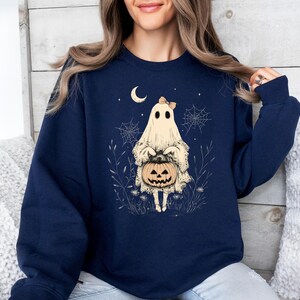 May include: A navy blue sweatshirt with a graphic of a ghost holding a jack-o'-lantern. The ghost is wearing a bow and has a friendly expression.
