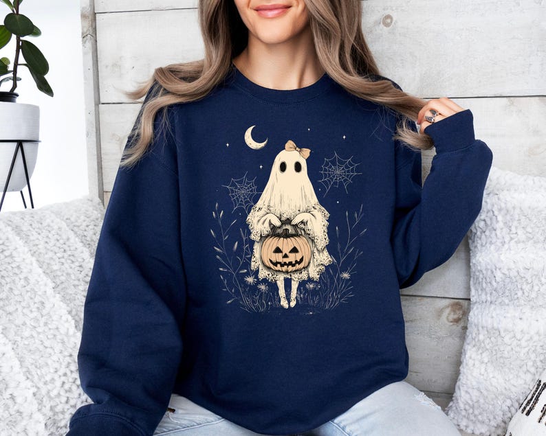 May include: A navy blue sweatshirt with a graphic of a ghost holding a jack-o'-lantern. The ghost is wearing a bow and has a friendly expression.