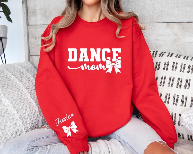 Pu&ograve; includere: Felpa rossa con il testo "Dance Mom" in bianco con un fiocco bianco. La manica sinistra ha il nome "Jessica" in bianco con un fiocco bianco.