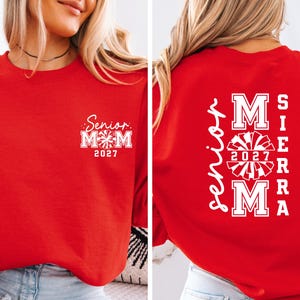 May include: Red sweatshirt with white text and graphics. The front features "Senior Mom 2027" in a script font. The back displays "Sierra Mom 2027" with a cheerleader graphic.