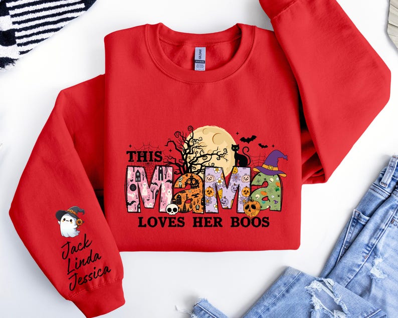 May include: Red sweatshirt with a Halloween-themed design that says "This Mama Loves Her Boos". The design features a black cat, a witch's hat, and a full moon. The sleeve has a ghost with a witch's hat and the names Jack, Linda, and Jessica.