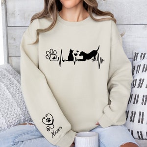 May include: A beige sweatshirt with a black paw print, cat, dog, and heartbeat graphic. The text "Name" is on the sleeve with a stethoscope graphic.