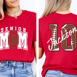 May include: A red t-shirt featuring a front graphic with the text SENIOR MOM and a football icon, and a back graphic with the large number 10, a football texture, and the name Jackson written in white script across the center of the number.